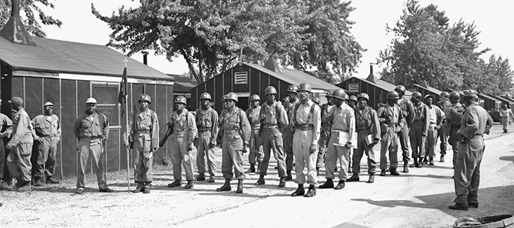 Black and white photo of soldiers standing in formation outside barracks.