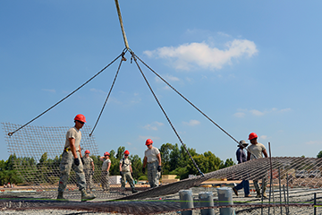 Members guide rebar sheets being lowered for the rebar cage used in foundation of a multipurpose building