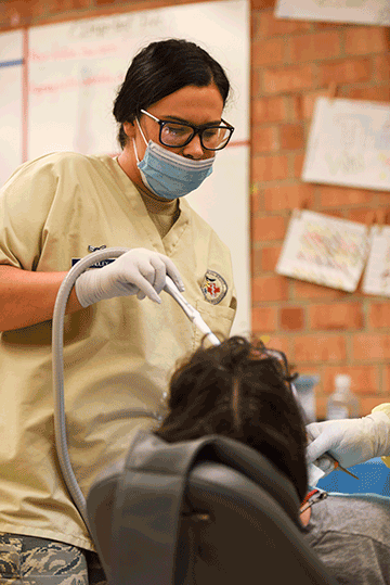 Airman 1st Class Carley Brindley provides suction during a dental procedure.
