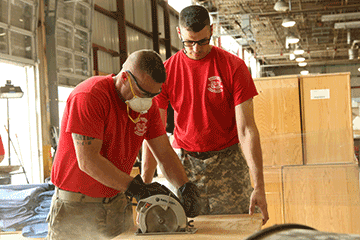 An Ohio Army National Guard Warrant Officer Candidate School student saws off excess material while his classmate steadies the wood.