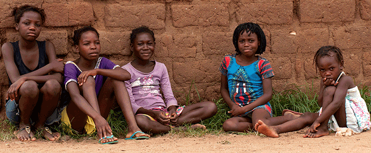 Children sit along brick wall in Angola.