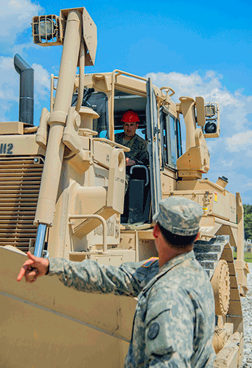 Sgt. John Musholt, a squad leader with the 1191st Engineer Company, gets guidance from the seat of a tractorized dozer at a parking lot construction site for the Unit Training Equipment Site (UTES) facility at Camp Ravenna Joint Military Training Center.