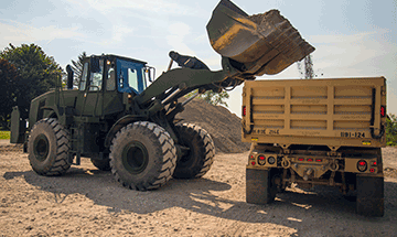 An front end loader, operated by the 1191st Engineer Company, drops a load of gravel for a waiting dump truck .