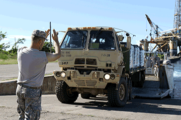 Spc. Anthony Daykin ground guides a truck carrying supplies onto an Army landing craft.