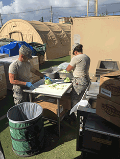Airmenpreparing food in outdoor kitchen.