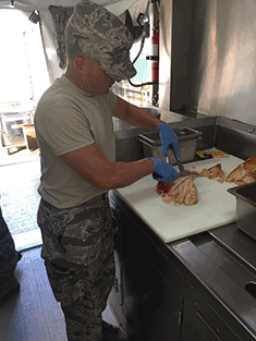 Airman cutting meat on board.