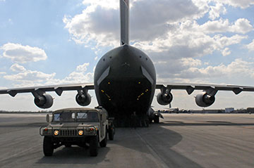 An Airman guides an Ohio Army National Guard Humvee onto a C-17 Globemaster III  humvee in fornt of aircraft.