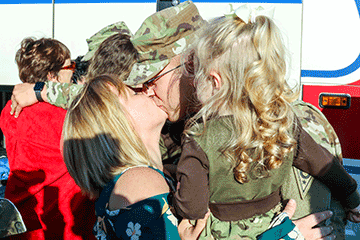 Soldier kisses loved one while holding girl.