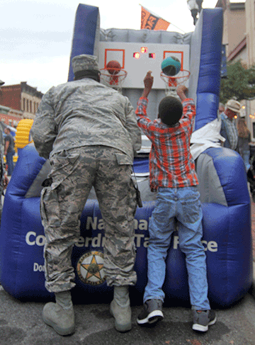 Guard member competing alongside boy in inflatable shoe-shaped basketball hoops game.