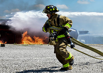 A firefighter with the Ohio Army National Guard’s 5694th Engineer Detachment rushes to unravel a fire hose with fire in background.