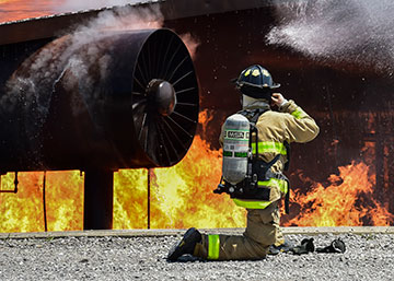 A firefighter with the Ohio Army National Guard’s 5694th Engineer Detachment straps on his fire helmet kneeling in front of fire.