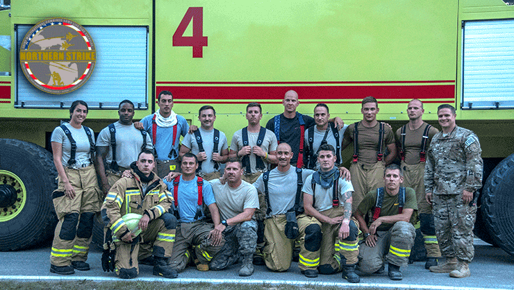 Staff Sgt. Andrea Villegas stands in front of firetruck with firefighters from the Alpena Combat Readiness Training Center, Ohio National Guard, Tennessee National Guard, Latvia, Estonia and Bulgaria.