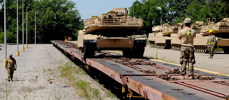 A Soldier with the Ohio Army National Guard’s 1st Battalion, 145th Armored Regiment ground guides a M1A1 Abrams tank off a train bed with additional tanks on road to the right that have already been off loaded.