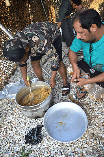 Local men making rice dish in pan on floor of tent.