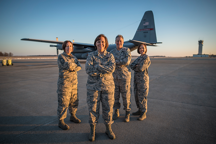 Female airmen stand with arms crossed on tarmack with c-130 in background