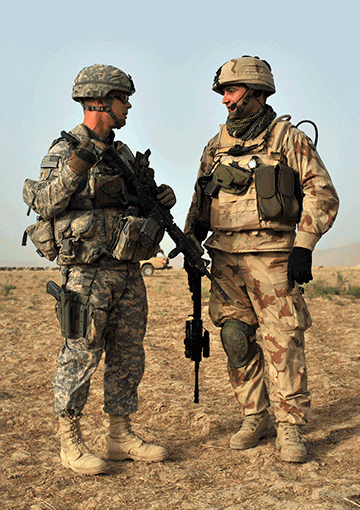 Soldiers standing in gear outside talking.