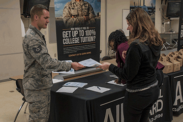 Alexander hands out materials to female recruit at table display.