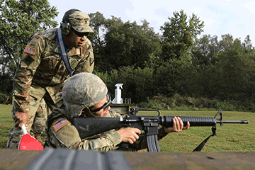 Soldier kneeling while shooting rifle while Soldier observes standing overtop.