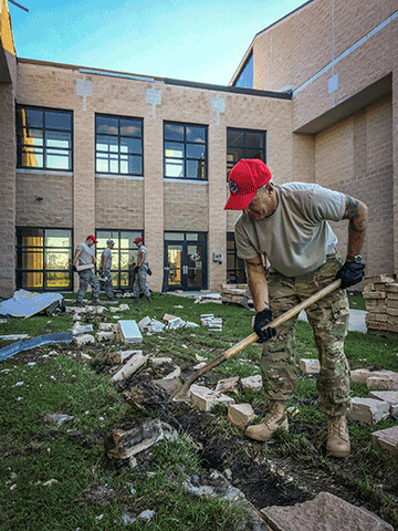 Airmen pick up brick debris from hurricane.