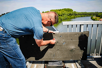 Soldier places patch into plaque on bridge above river.