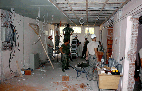 Ohio National Guard airmen work inside room with cables hanging from ceiling and rubble all around.