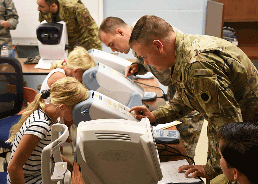 Ohio National Guard medical personnel provide vision examinations with children using machines on tables.