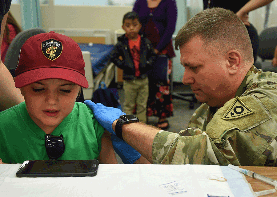Soldier gives a child an immunization shot.