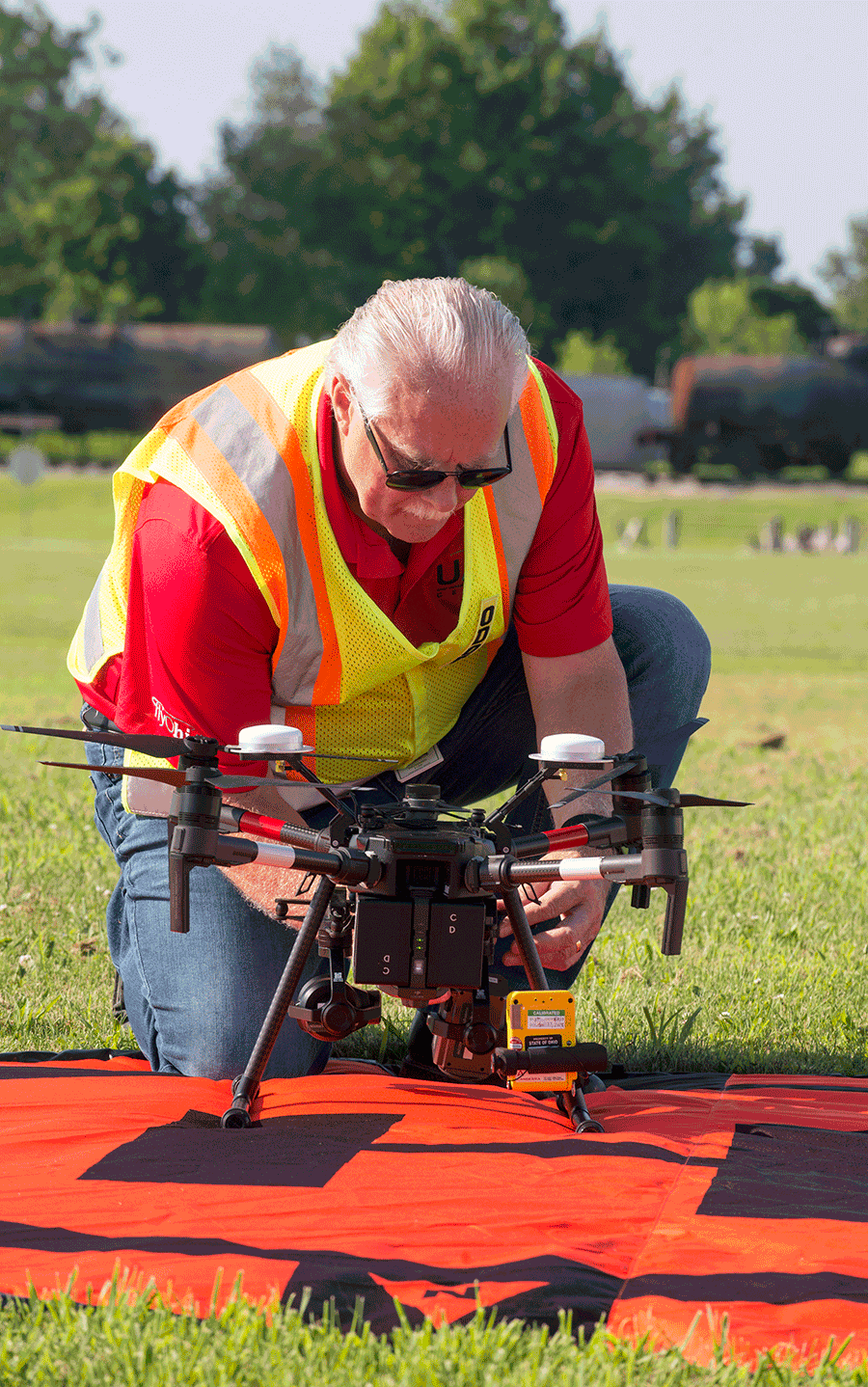 Man with orange vest kneels on orange landing pad to calibrate a reconnaissance drone.