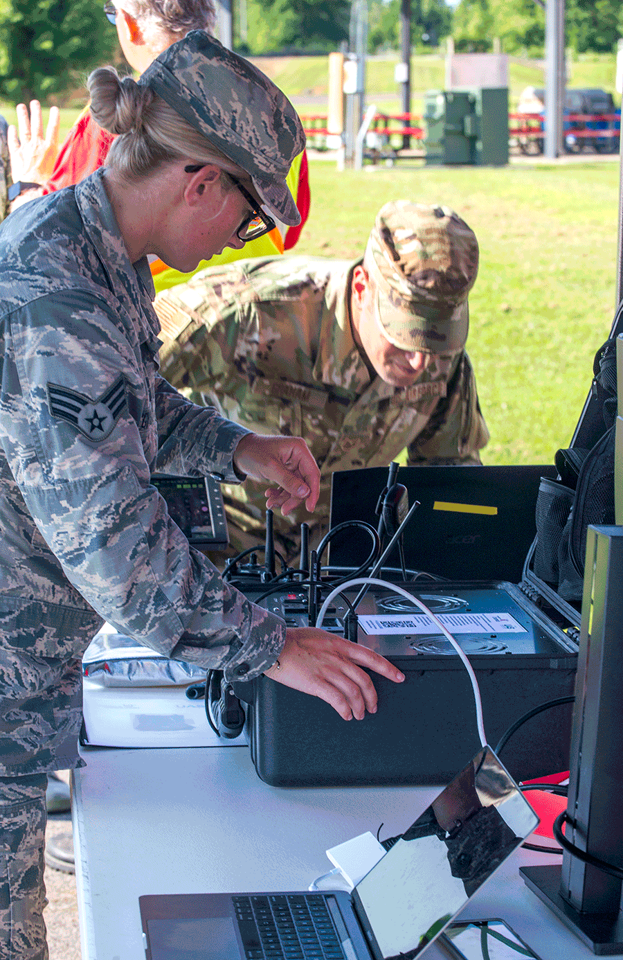 Female Airman sets up communication equipmenton table under tent in field.
