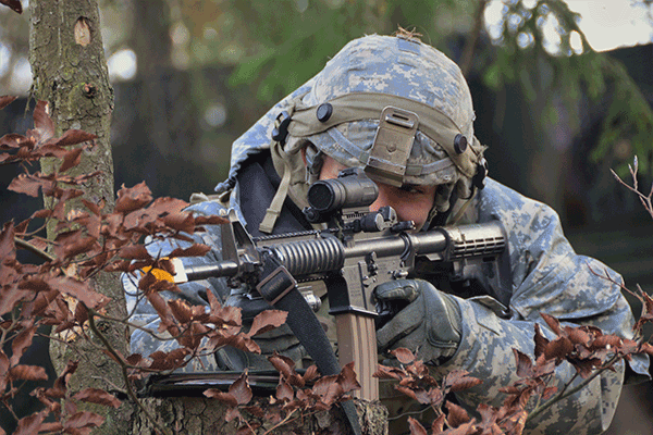 Soldier looks through scopeon weapon in woods