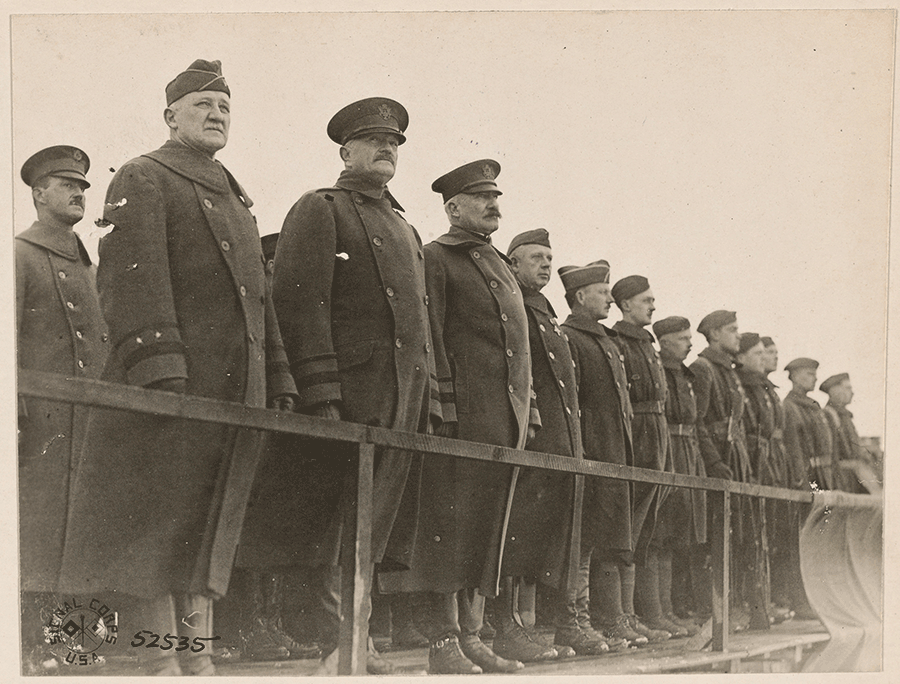 Sepia tone image of senior leaders standing in stands outside.