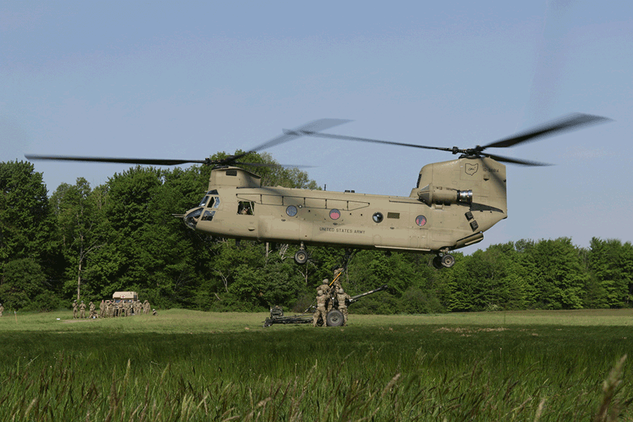 Soldiers attach an M777 howitzer to the underside of a CH-47 Chinook helicopter
