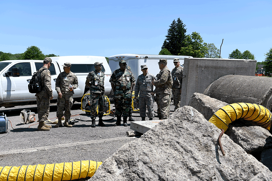 Soldiers gather around truck/trailer at simulated concrete rubble disaster area.