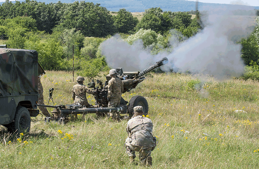 Soldiers fire M119A3 howitzer in field.