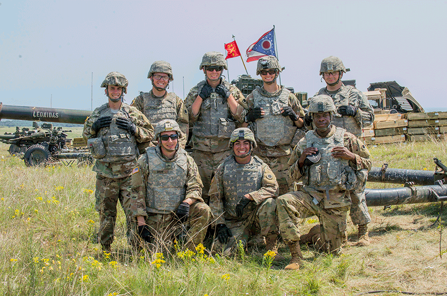 Soldiers stand for group pic with flags in background.
