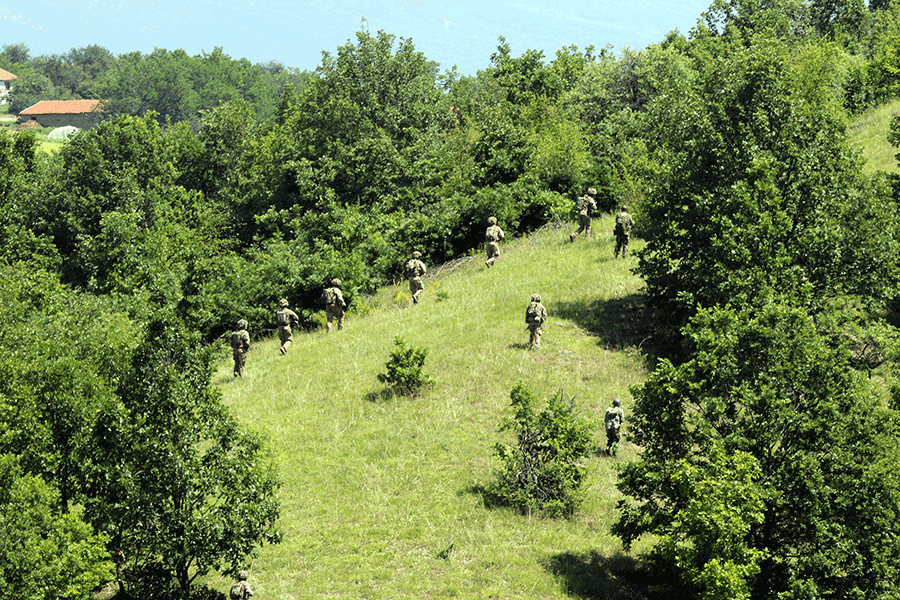 Aerial view of Soliders in clearing of treed area.