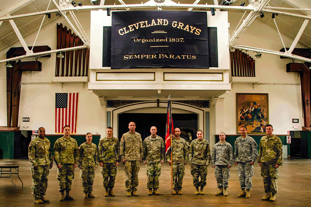 Soldiers stand at attention in line under Cleveland Grays flag.