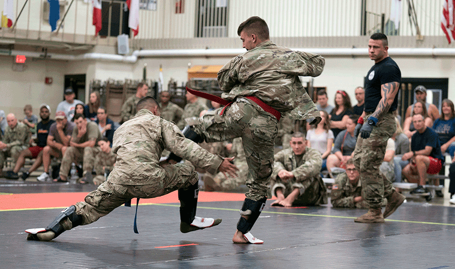 Soldiers compete on mat while others observe match.