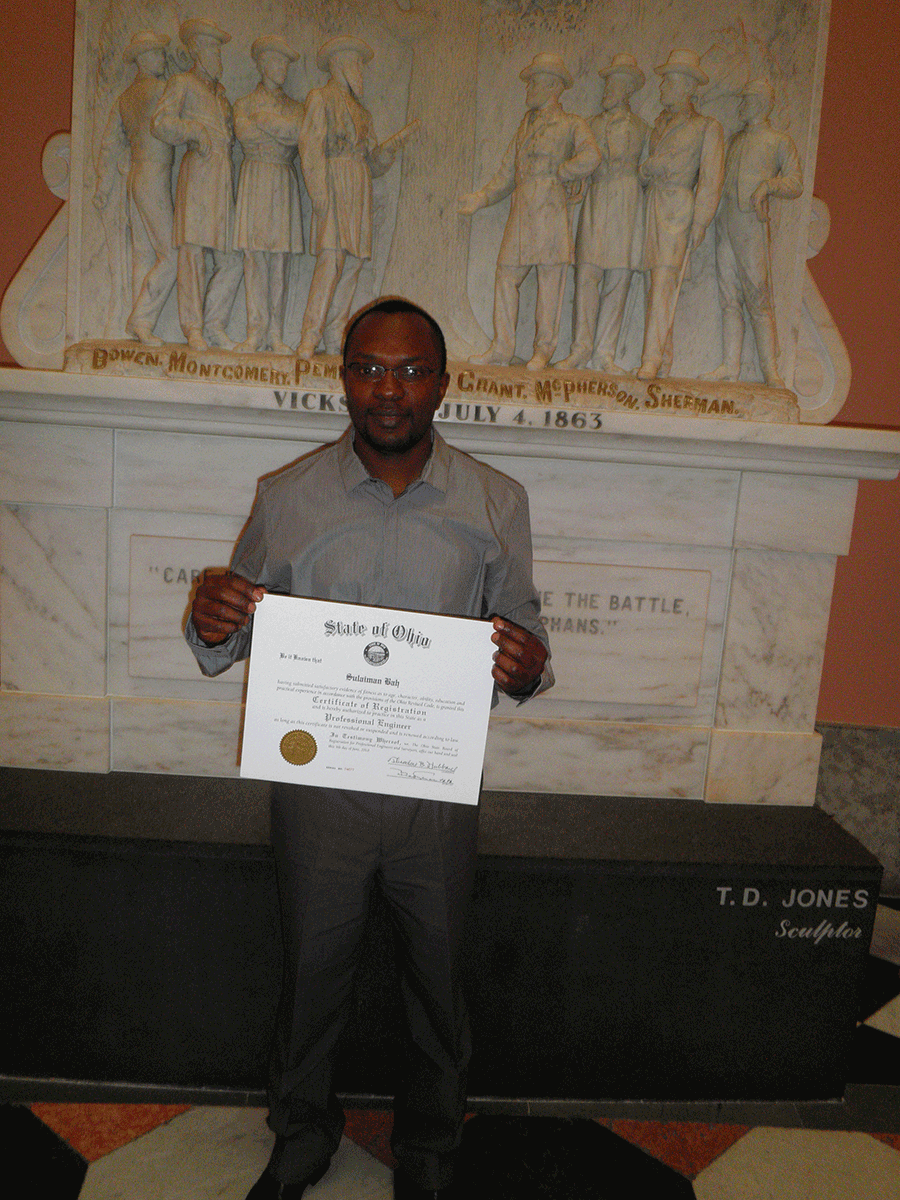 CBah holds certificate in front of statue.