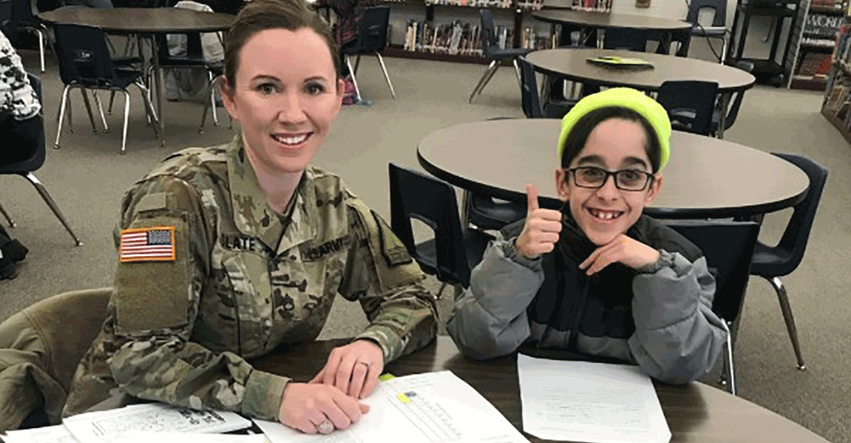 Sgt. 1st Class Nena Slate at table with young girl in library.