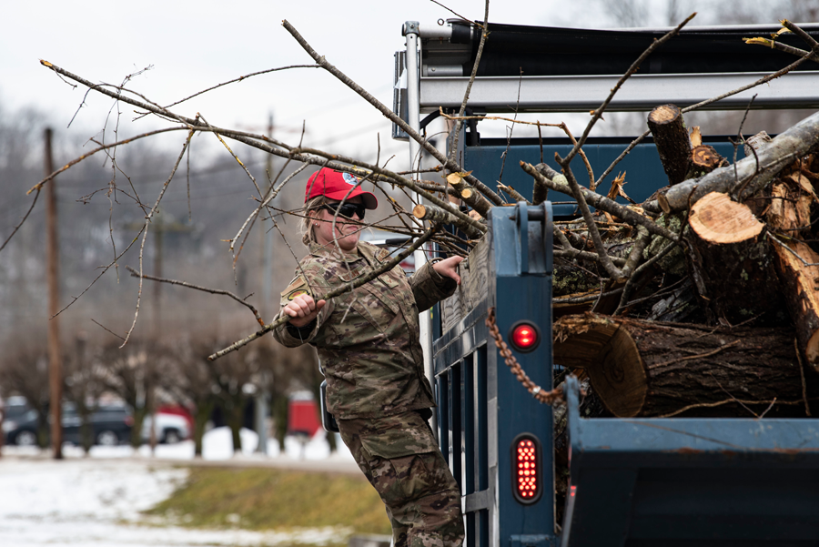 Female soldier loads branches into truck.