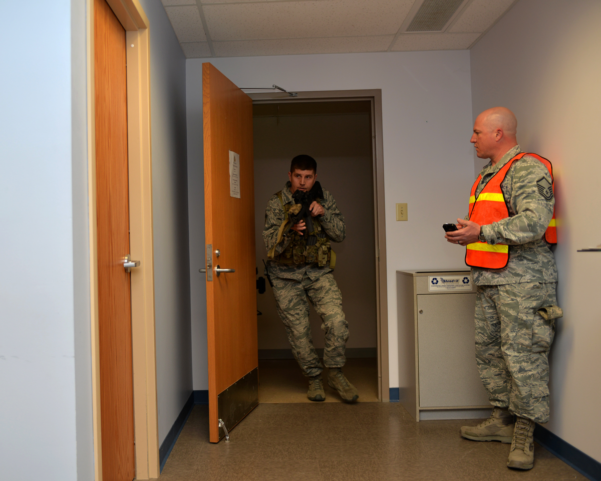 Chief Master Sgt. Troy Taylor coming through open door in room with weapon while being timed by member in orange vest. 