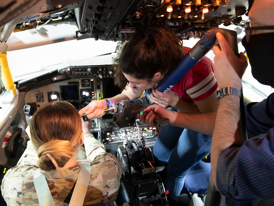 Woman checks female pilot's distance to controls in cockpit.