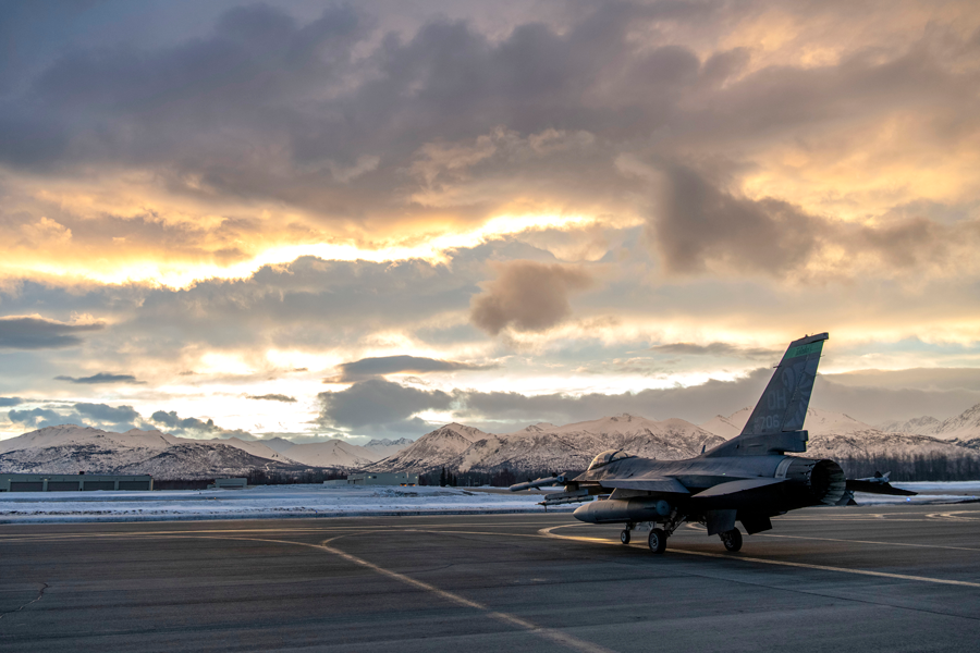 F-16 taxis on runway at dawn in Arctic mountains in the distance.