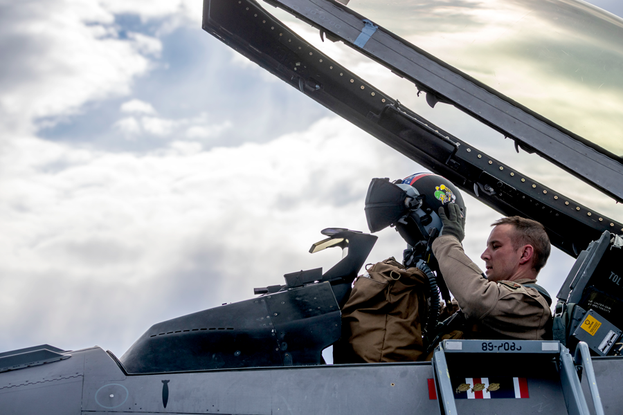 Airman in F-16 with top off, removing helmet.