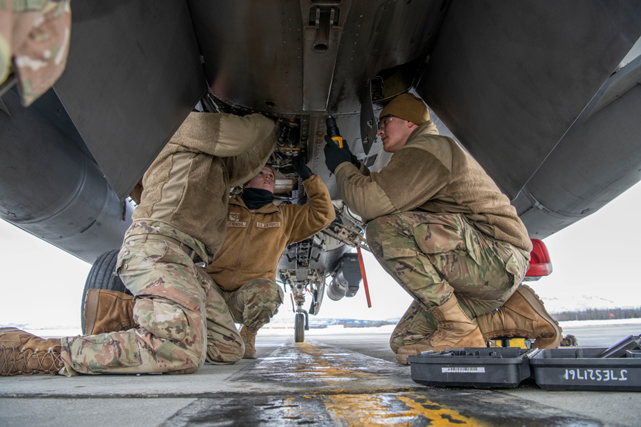 Airmen inspect engine underneath F-16.
