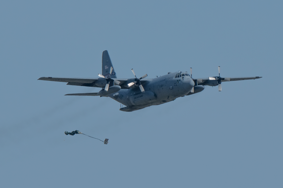An airborne C-130H Hercules drops its cargo.