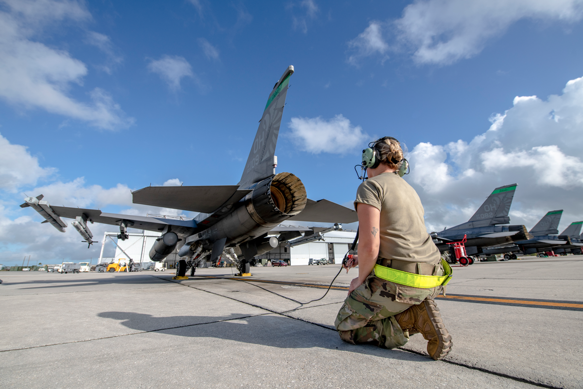 Female crew chief on tarmac inspecting F-16.
