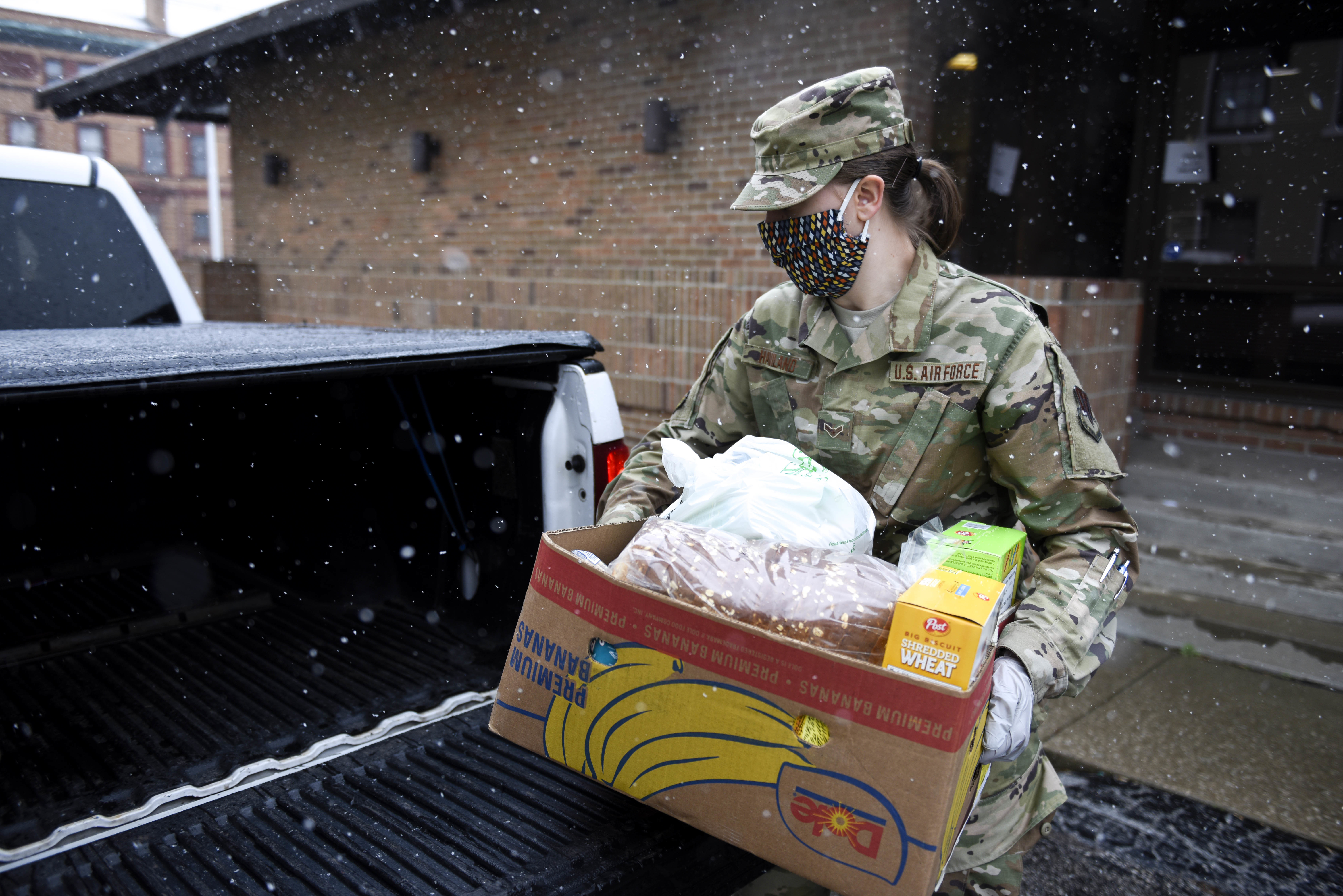 FEmale soldier loads box into back of a truck in the snow.