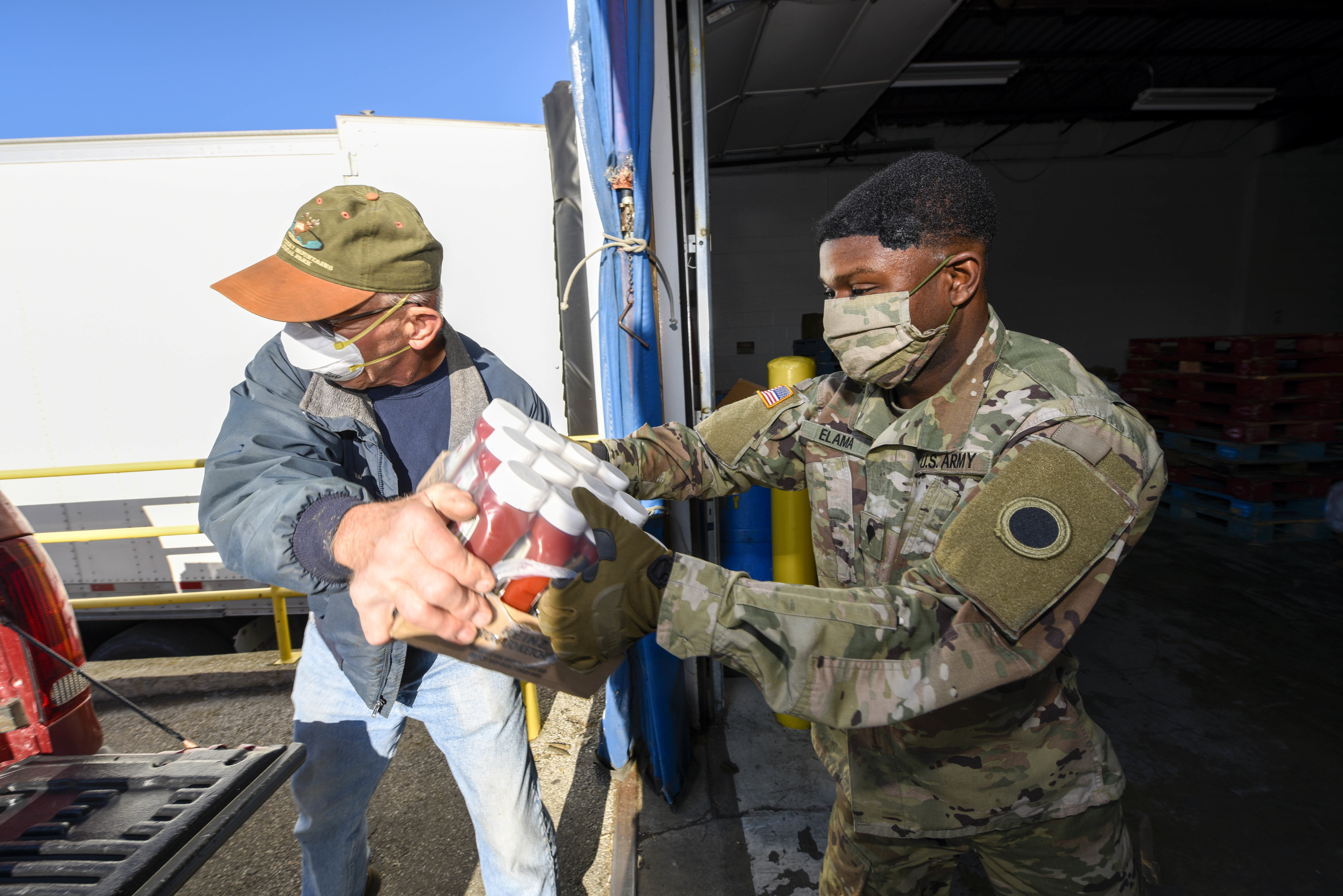 Soldier hands groceries to man to load in back of truck.